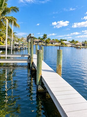 A wooden dock extending into calm water, surrounded by palm trees and buildings with thatched roofs. - 3-bedroom house in gorgeous Cape Coral with pool and deck (Cape Coral)