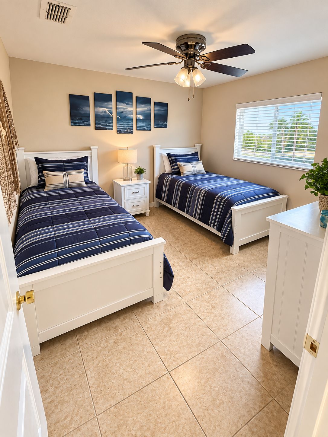 A bedroom with two beds, a ceiling fan, a window with blinds, and artwork on the wall.