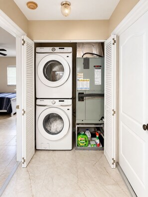 A laundry room with two stacked washing machines, a utility cabinet with safety instructions, and a shelf with cleaning supplies. - 3-bedroom house in gorgeous Cape Coral with pool and deck (Cape Coral)