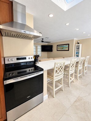 A modern kitchen with a stainless steel range, a built-in oven, and a dining area with white chairs. - 3-bedroom house in gorgeous Cape Coral with pool and deck (Cape Coral)