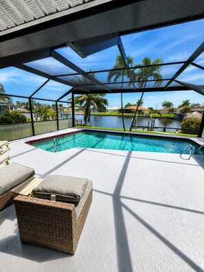 An outdoor swimming pool with a view of a lake and palm trees, surrounded by a covered area with seating. - 3-bedroom house in gorgeous Cape Coral with pool and deck (Cape Coral)