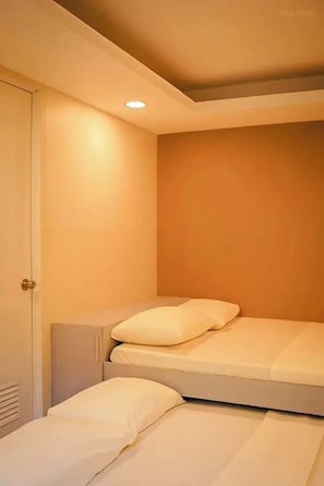 Una habitación pequeña con cama individual, puerta e iluminación en el techo.