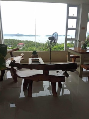 A room with a view of the sea, a fan, and a table with chairs.