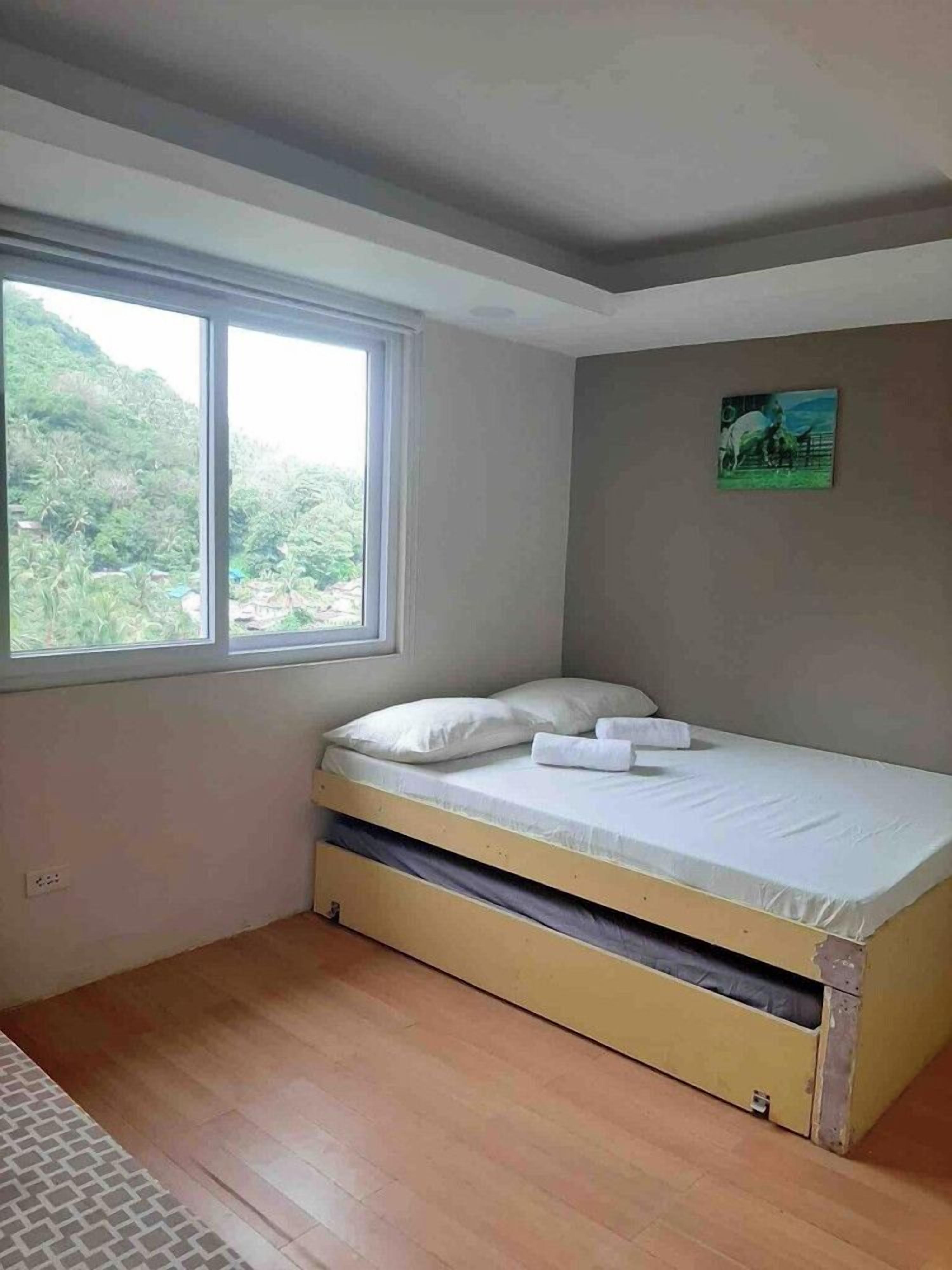 A single bed with a mattress and pillows in a room with a window and a painting on the wall.