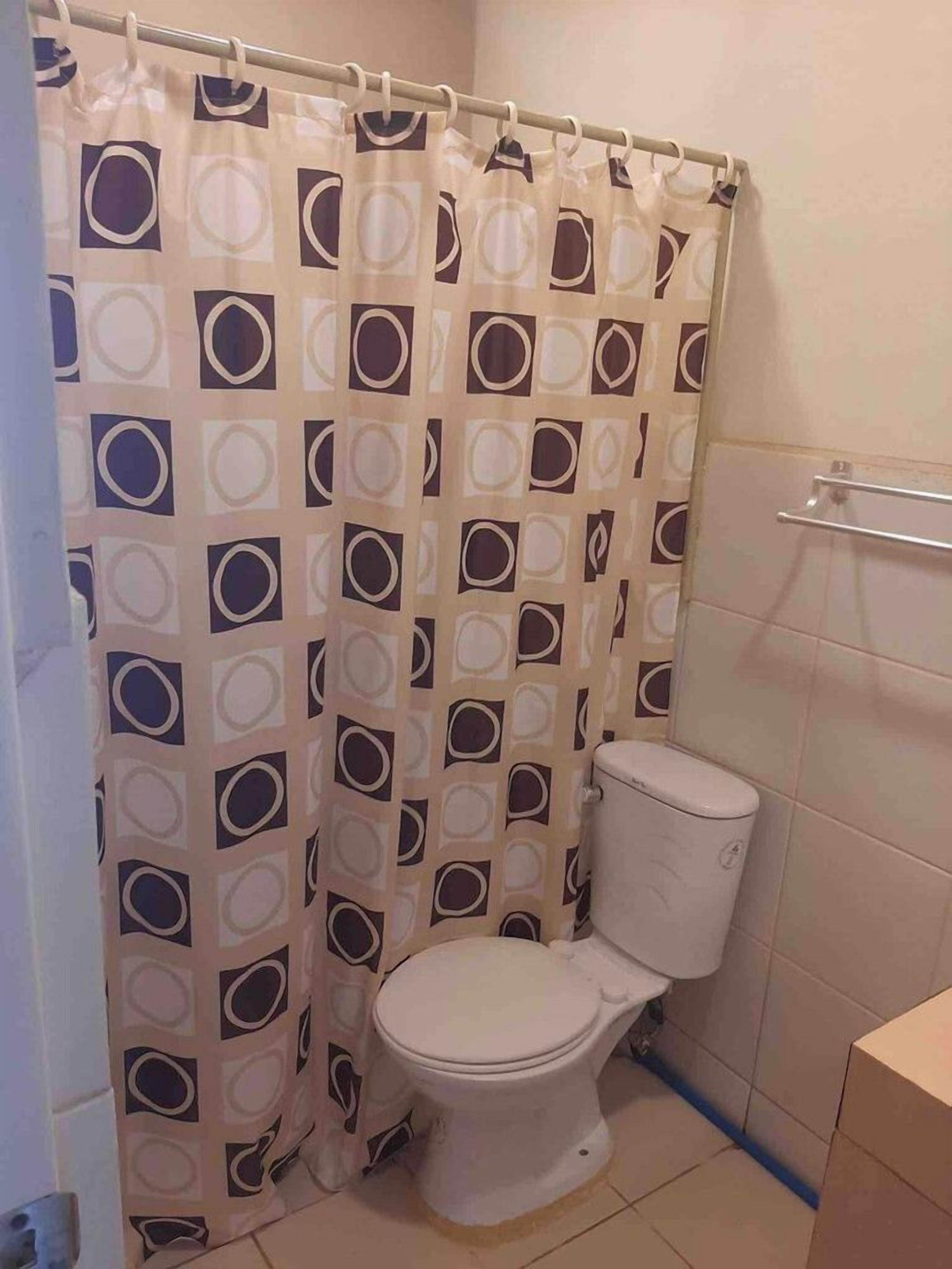A bathroom with a toilet, a shower curtain with a geometric pattern, and a tiled wall.