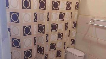 A bathroom with a toilet, a shower curtain with a geometric pattern, and a tiled wall.