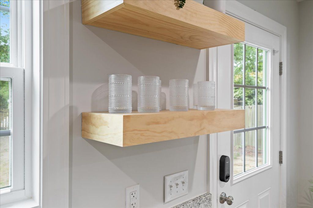 Een houten plank met transparante glazen potten tegen een witte muur, een deur met raam en een deurbel.