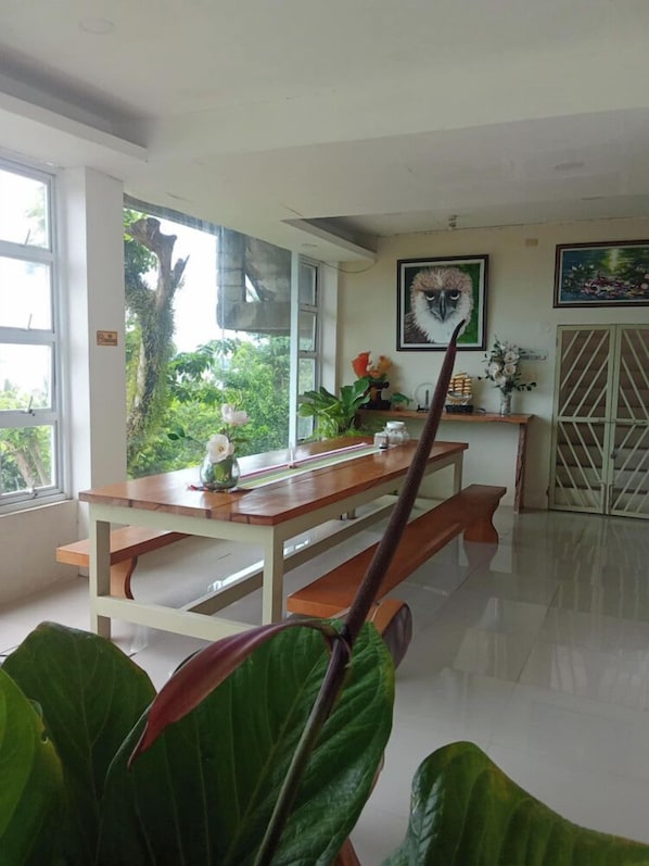 A dining area with a wooden table and benches, a window with a view of greenery, and a door with a metal gate.