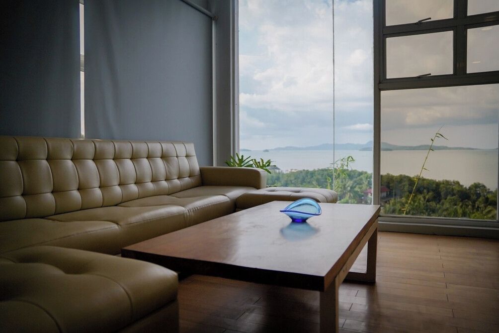 Ein modernes Wohnzimmer mit einem Ledersofa, einem Holztisch und Blick auf ein Gewässer durch große Fenster.