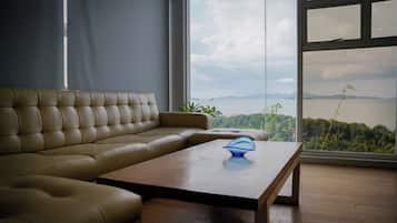Ein modernes Wohnzimmer mit einem Ledersofa, einem Holztisch und Blick auf ein Gewässer durch große Fenster.