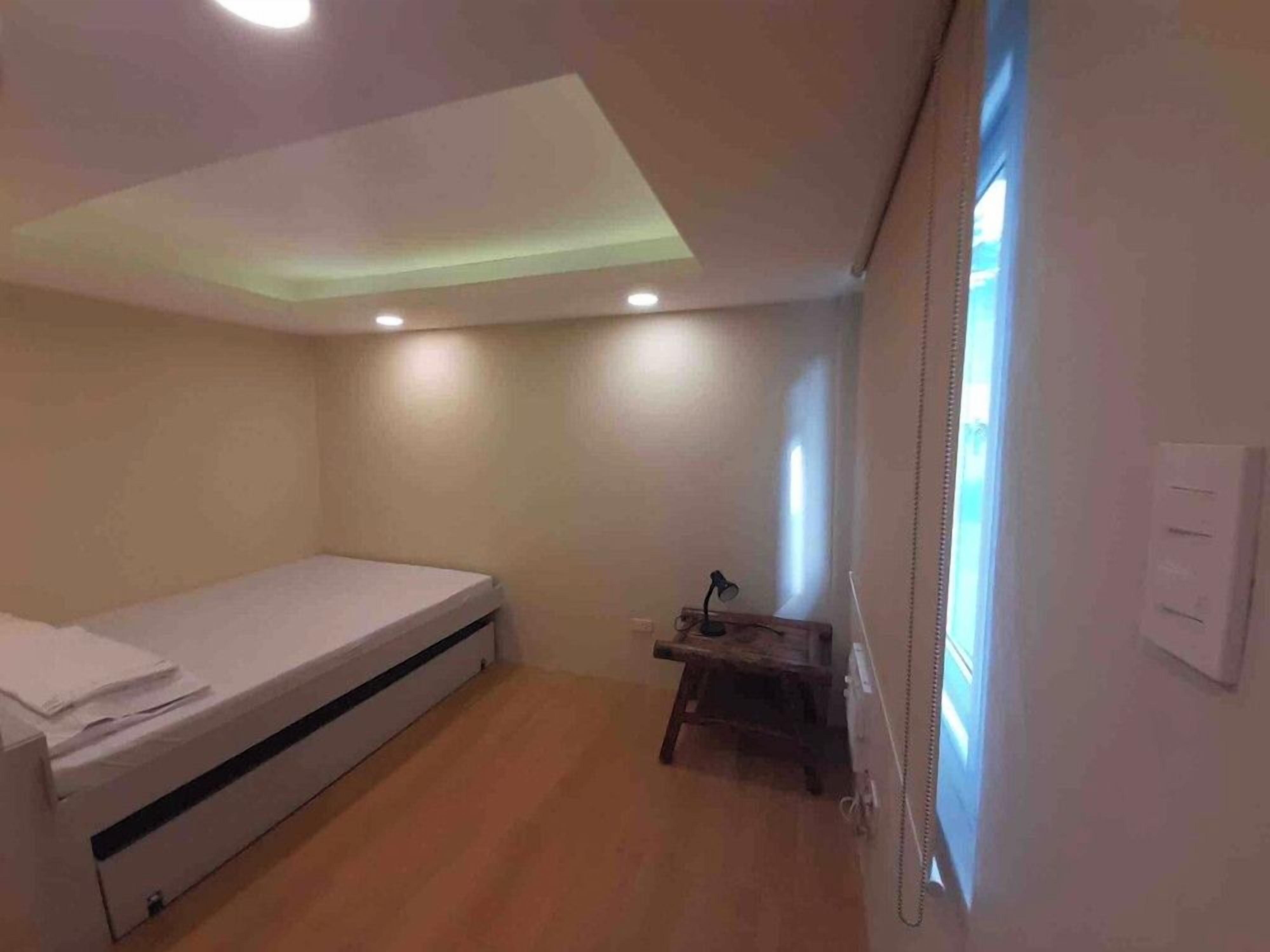 A compact room with a bed, a small desk, and a window with blinds.