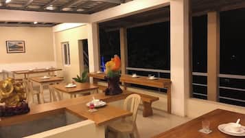 A dining area with wooden tables and chairs, a decorative centerpiece, and large windows.