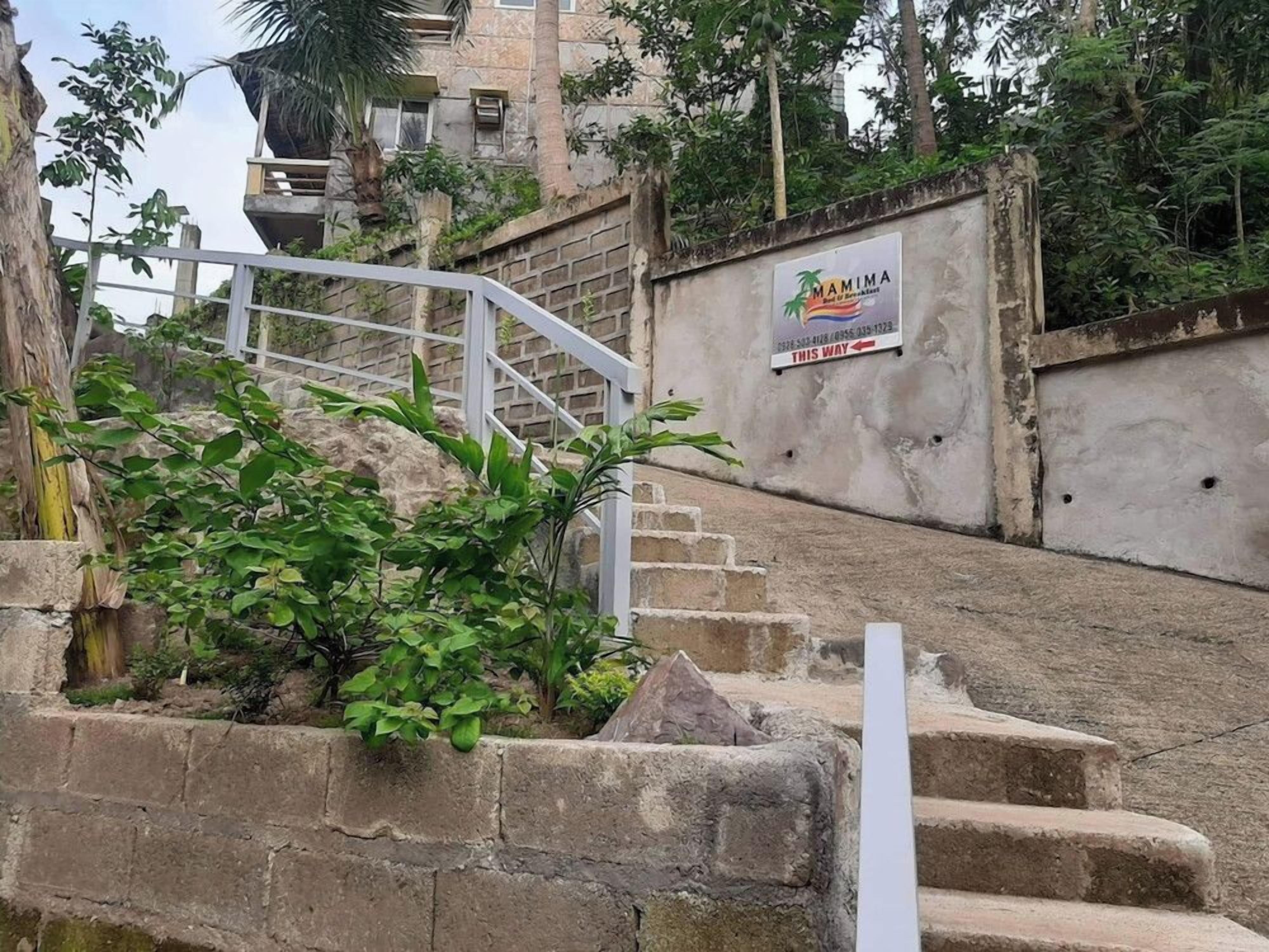 Un escalier menant à un bâtiment sur lequel est apposée une enseigne indiquant « MAMIMA ».