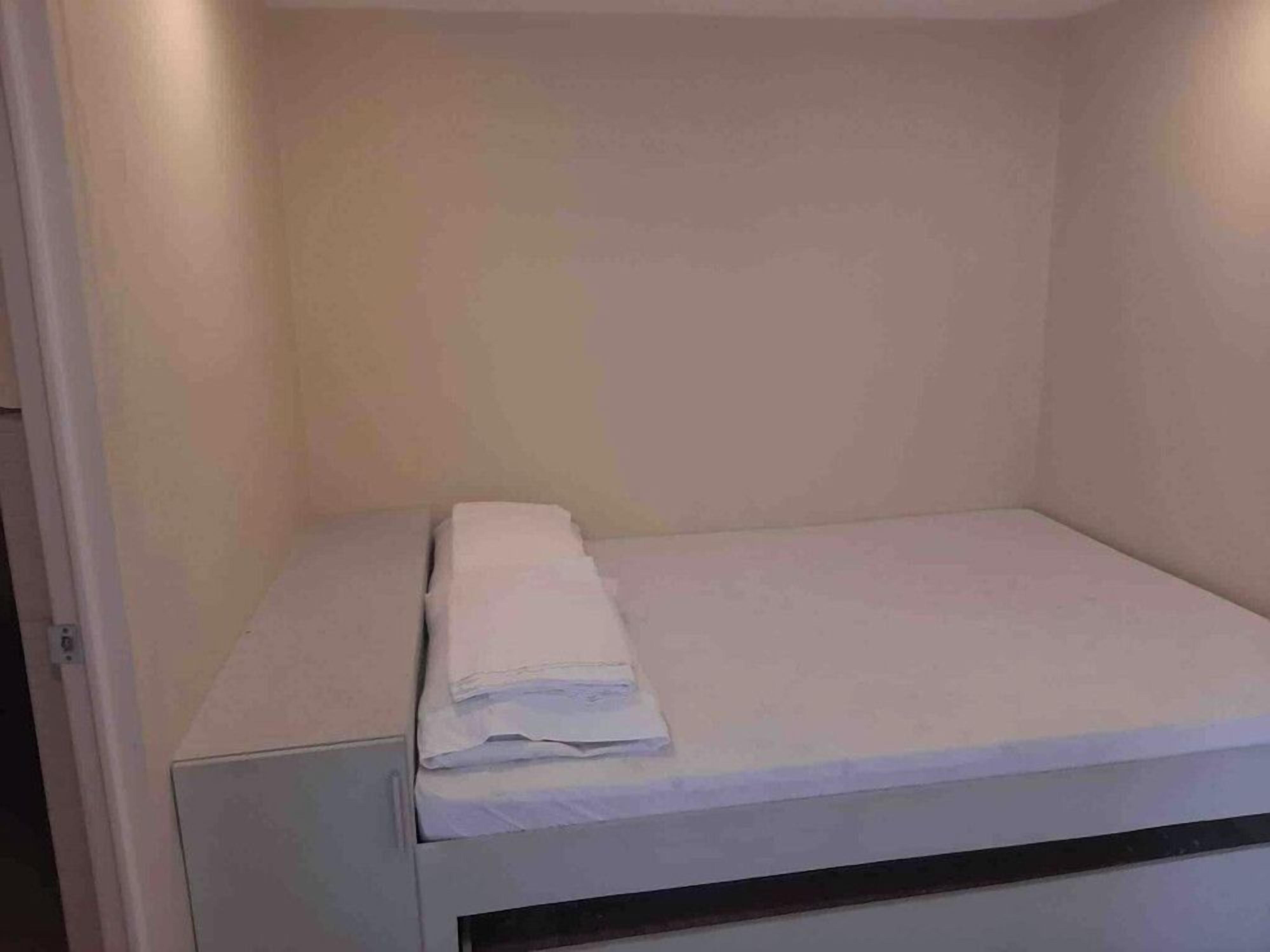 Ein kleines Zimmer mit einem Einzelbett, einer weißen Matratze und einer ordentlich gefalteten weißen Decke.