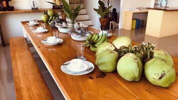 A long wooden table with plates, cups, and a glass, and a large number of green coconuts.