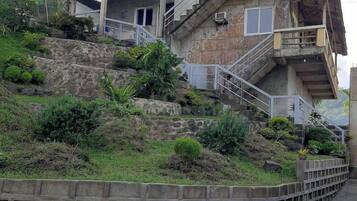 Un immeuble à plusieurs étages, doté d’un escalier menant à l’étage supérieur, entouré de verdure et bordé d’un mur de soutènement.