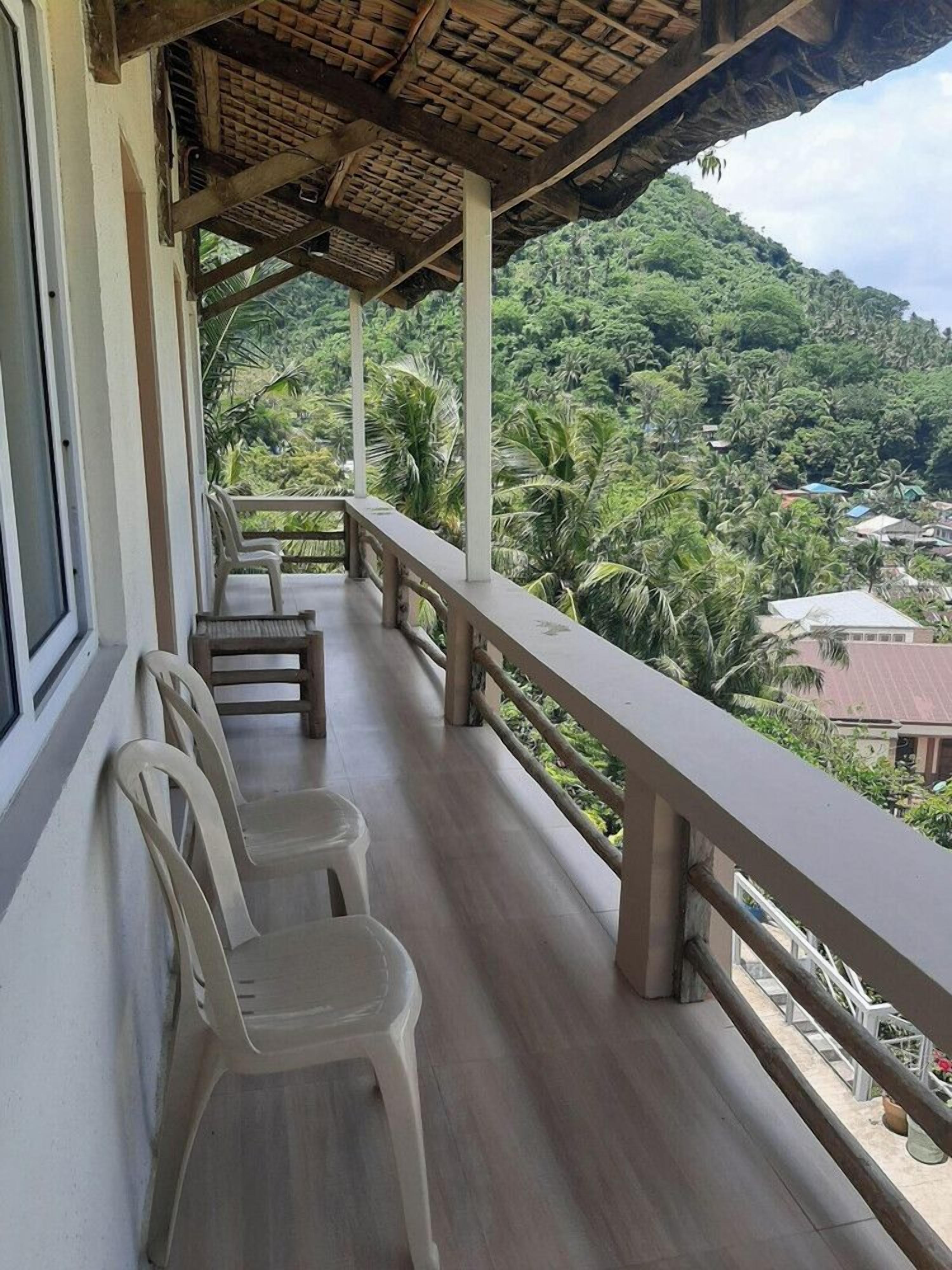 Un balcon avec des chaises en plastique et une balustrade en bois, donnant sur un paysage verdoyant et luxuriant.