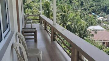 Un balcon avec des chaises en plastique et une balustrade en bois, donnant sur un paysage verdoyant et luxuriant.