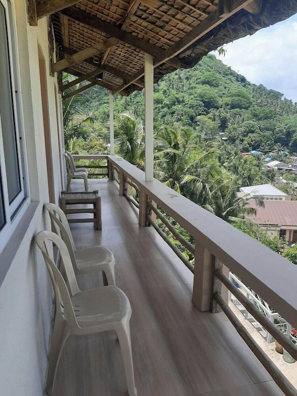 Un balcón con sillas de plástico y baranda de madera con vista a un paisaje verde exuberante.