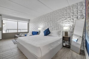 A modern hotel room with a large bed, a geometric patterned wall, a bedside table with a lamp, and a view through a window. - Enchanting Disney Stay + Free Parking & Pool (Kissimmee)