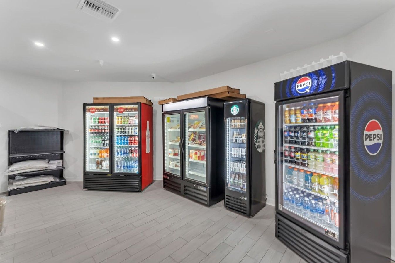 Una hilera de máquinas expendedoras de bebidas en una habitación con piso de baldosas y pared blanca.