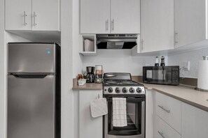 Een functionele keuken met een koelkast van roestvrij staal, een gasfornuis, een magnetron en een koffiezetapparaat op het aanrecht.