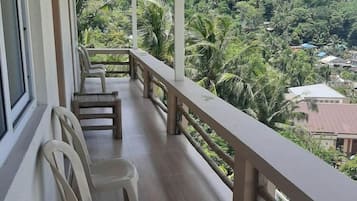 Een balkon met plastic stoelen, een houten vloer en uitzicht op een weelderig groen landschap.