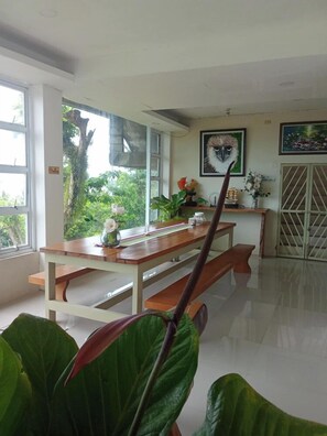 A dining area with a wooden table and benches, a window with a view of greenery, and a door with a metal gate.