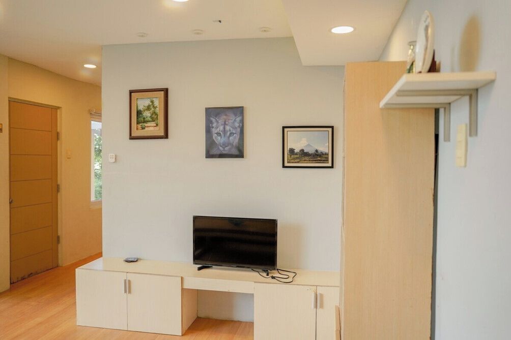 Une pièce avec un téléviseur posé sur un meuble, un buffet et trois tableaux encadrés accrochés au mur.