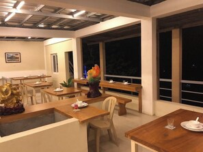 Un área de comedor con mesas y sillas de madera, un centro decorativo y ventanas amplias.