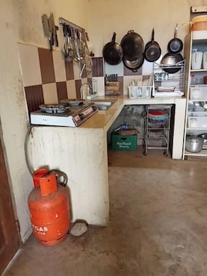 A kitchen with a gas stove, hanging utensils, and a gas cylinder.