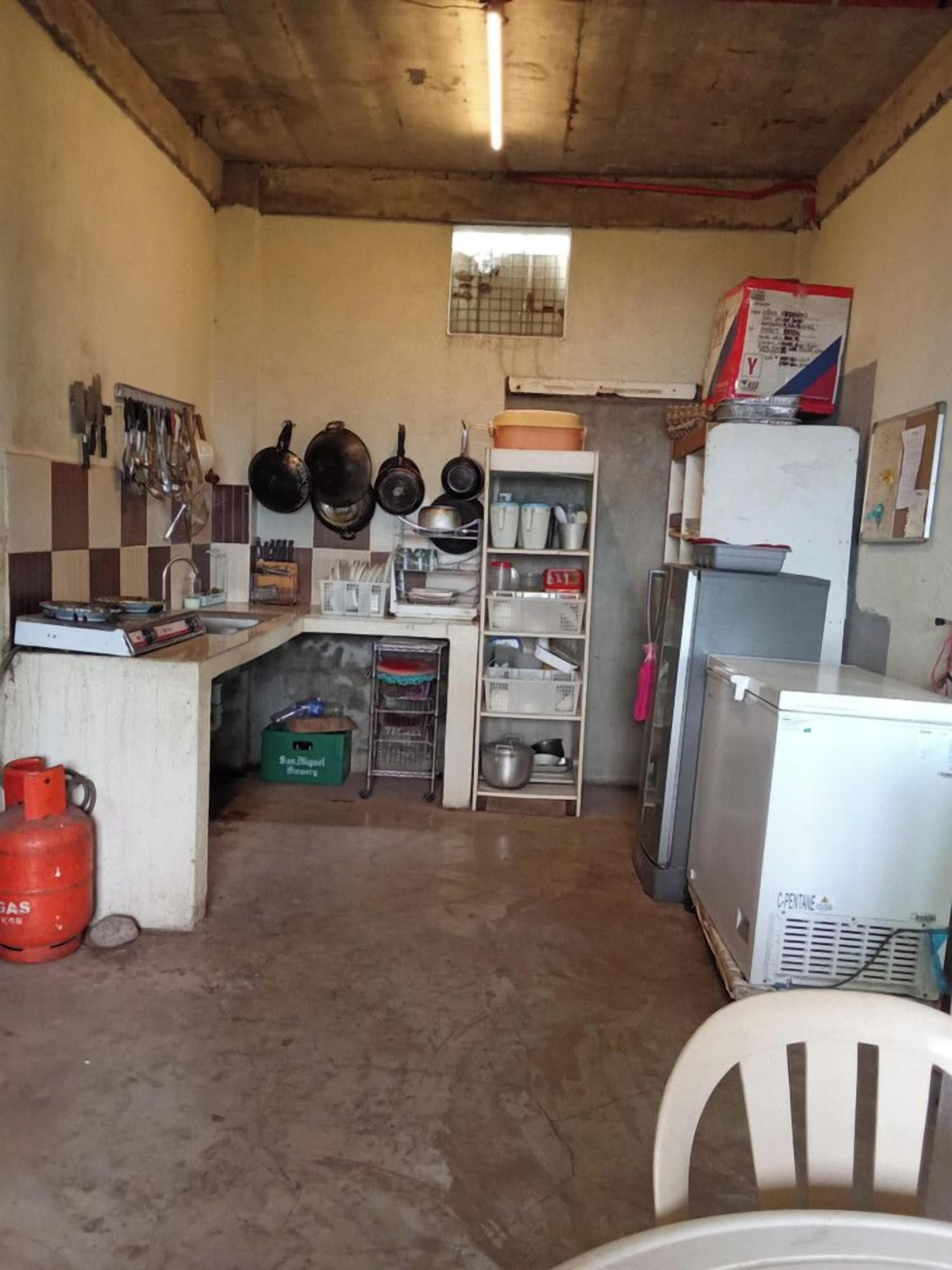 A compact kitchen with basic amenities, including a sink, a refrigerator, and a gas cylinder.