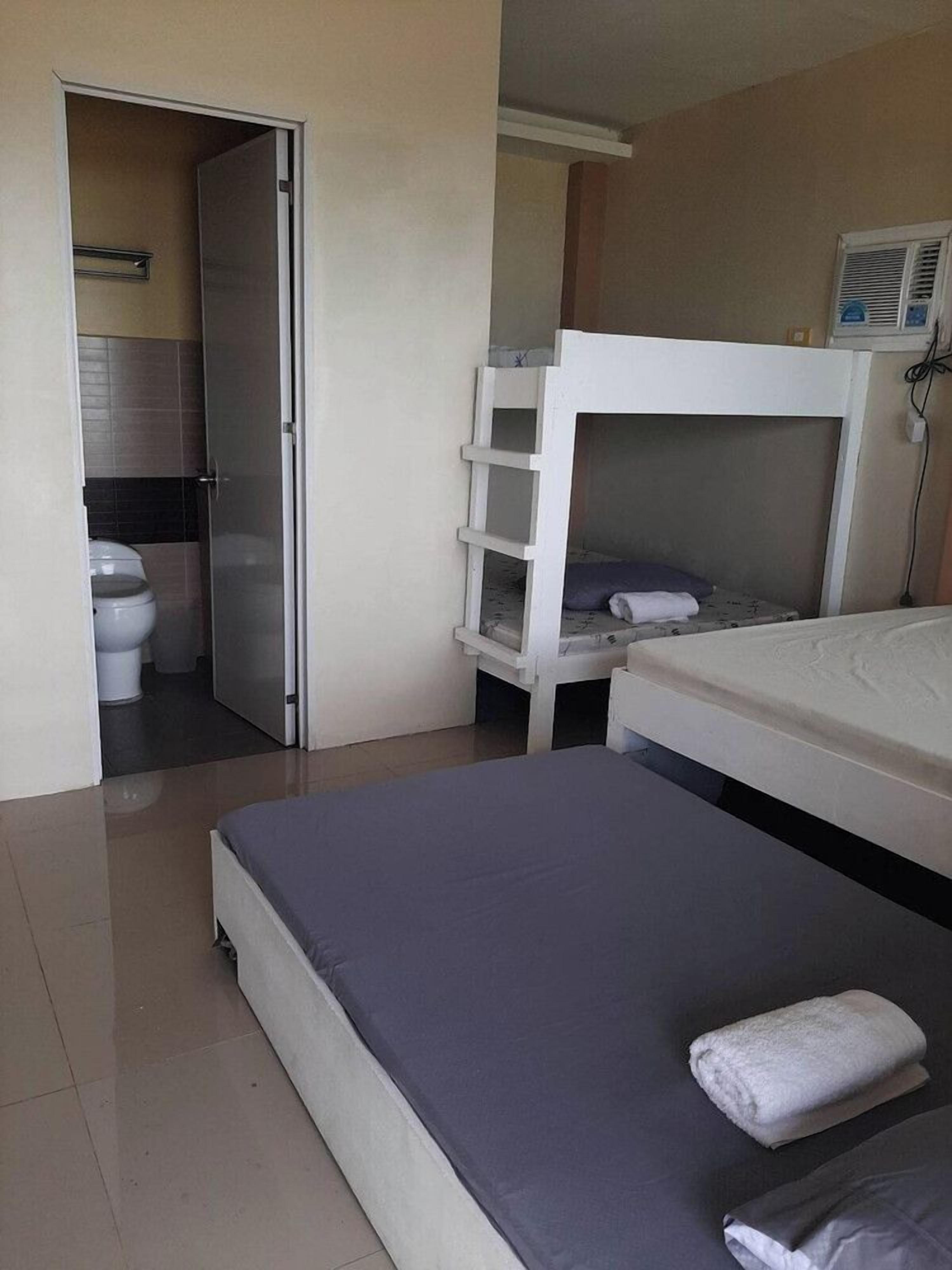 A room with a bunk bed, a single bed, a bathroom with a toilet and shower, and a door leading to another room.