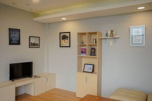 A living room with a flat-screen TV, a wooden cabinet, a bookshelf, and a cushioned bench.