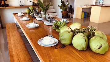 Een lange houten tafel met borden, bekers en een glas, en een groot aantal groene kokosnoten.