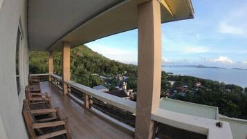 A balcony with wooden chairs, a view of a coastal town, and a clear sky.
