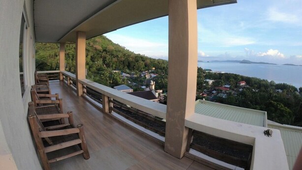 A balcony with wooden chairs, a view of a coastal town, and a clear sky. - Cozy Room at Mamima BnB (Caramoan)