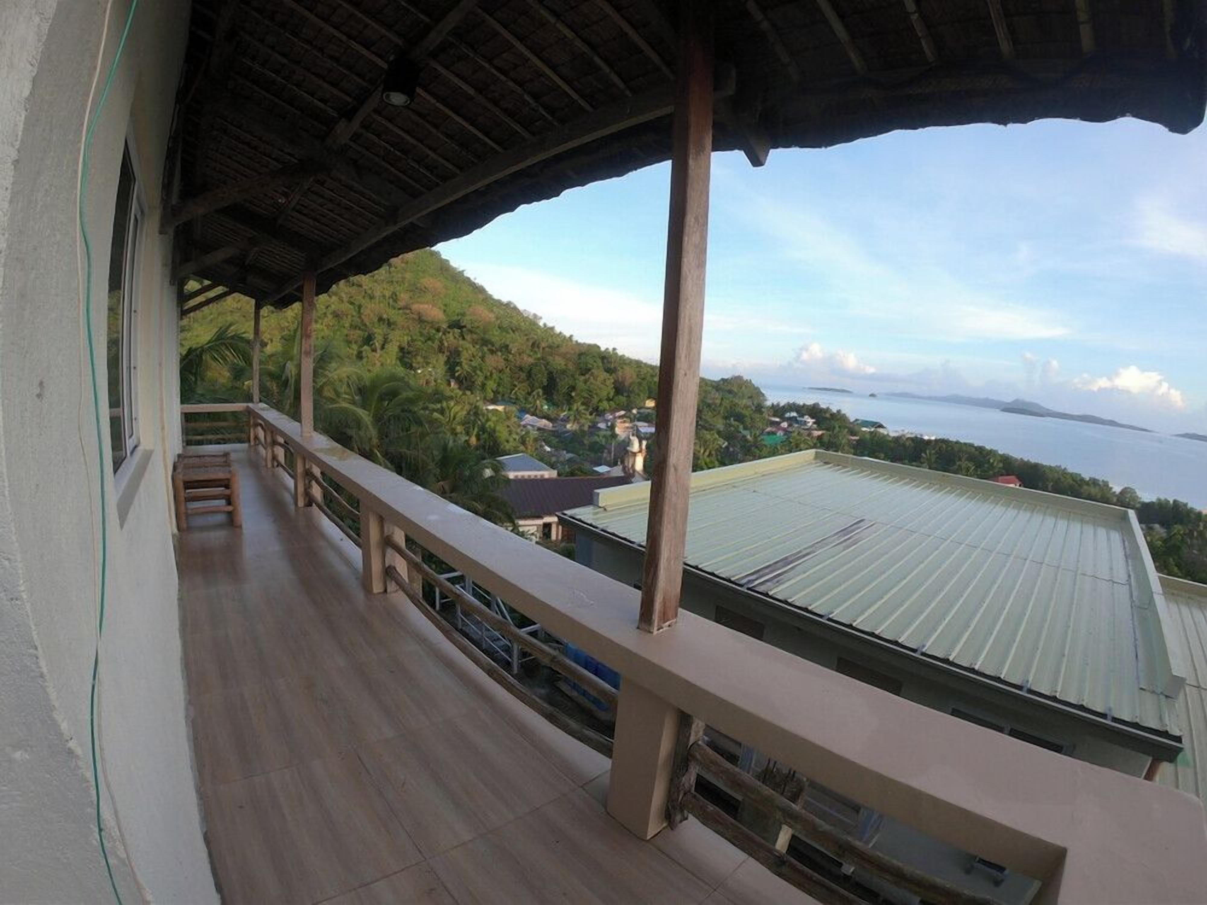 Un espace extérieur abrité, doté d’une terrasse en bois, d’une rambarde et offrant une vue sur un paysage verdoyant et une étendue d’eau.