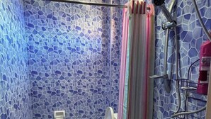 Een badkamer met een wand betegeld met mozaïek, een toilet, een douchegedeelte en een wastafel.