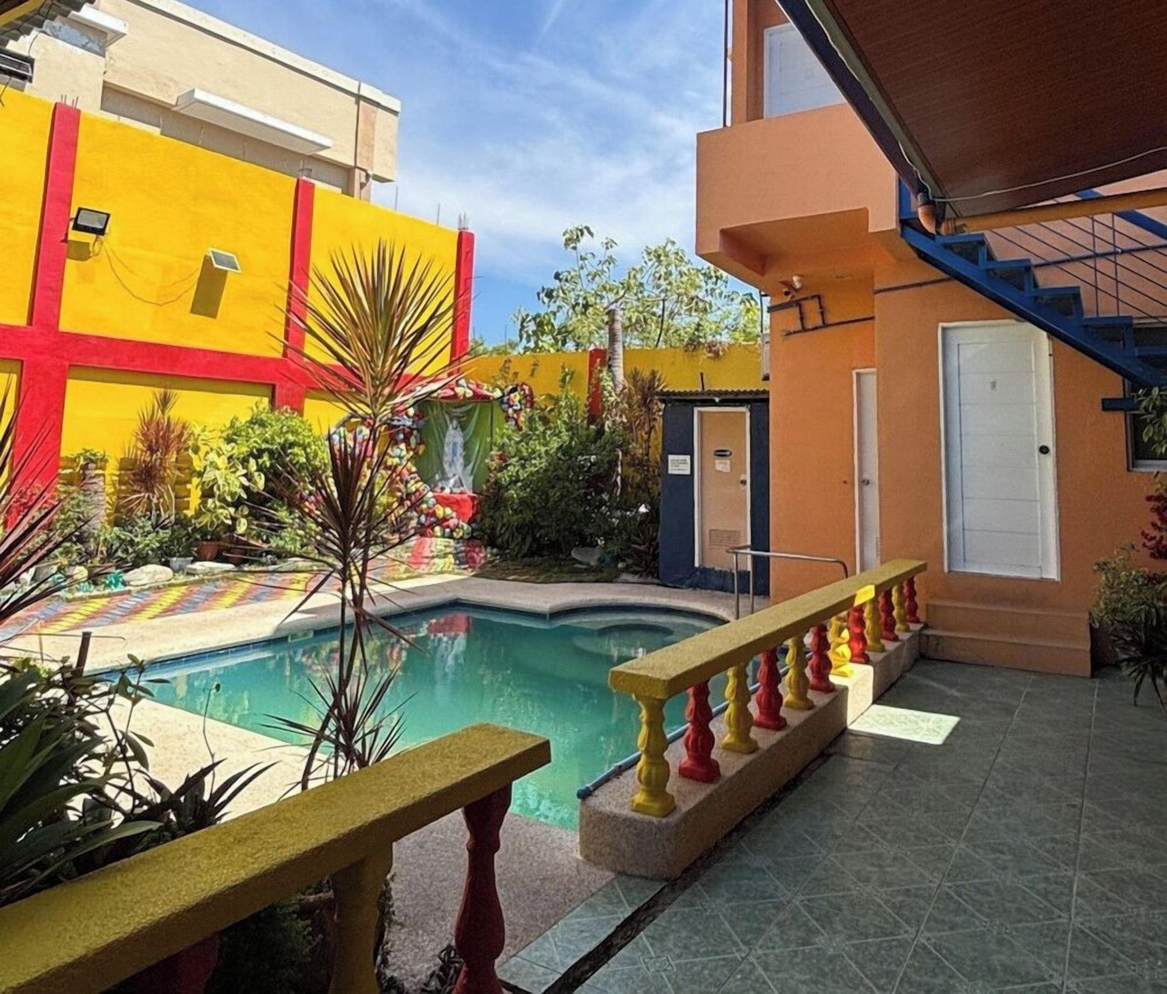A courtyard with a swimming pool, a small garden, and a building with a red and yellow facade.