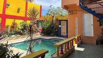 A courtyard with a swimming pool, a small garden, and a building with a red and yellow facade.