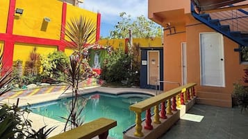 A courtyard with a swimming pool, a small garden, and a building with a red and yellow facade.