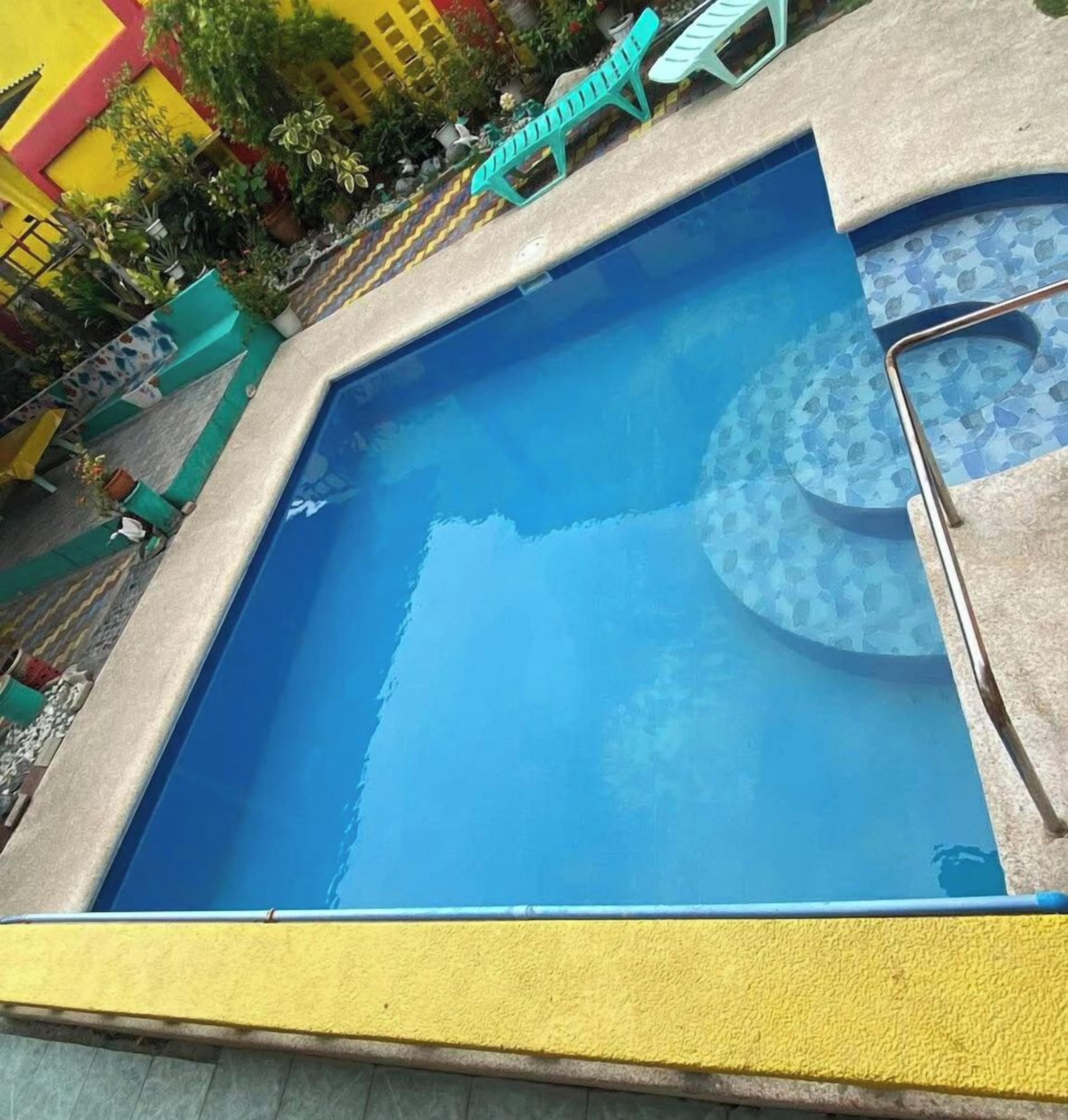Una piscina rectangular con superficie de agua azul cristalina, rodeada por una plataforma de concreto y un borde amarillo de seguridad.