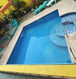 Una piscina rectangular con superficie de agua azul cristalina, rodeada por una plataforma de concreto y un borde amarillo de seguridad.