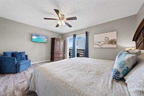 Ein Schlafzimmer mit einem Bett, einem Deckenventilator, einem Fernseher, einem Schrank und einem Fenster mit Vorhängen.