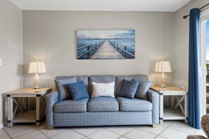 Ein Wohnzimmer mit einem grauen Sofa, zwei Beistelltischen mit Lampen und einem Gemälde eines Piers an der Wand.