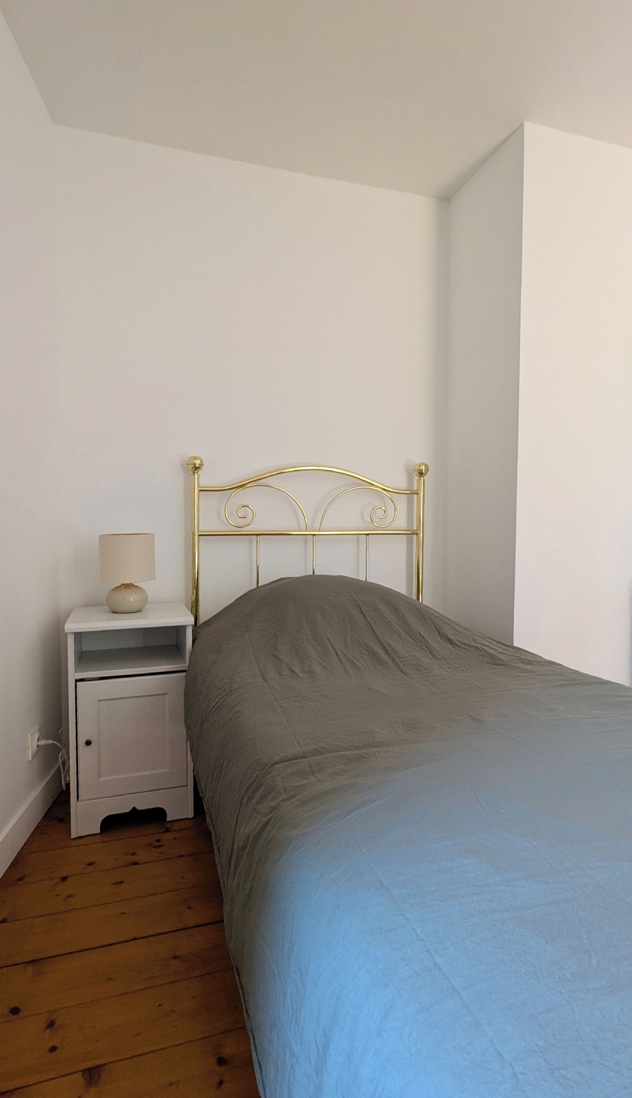 A bedroom with a single bed, a nightstand with a lamp, and a white wall.