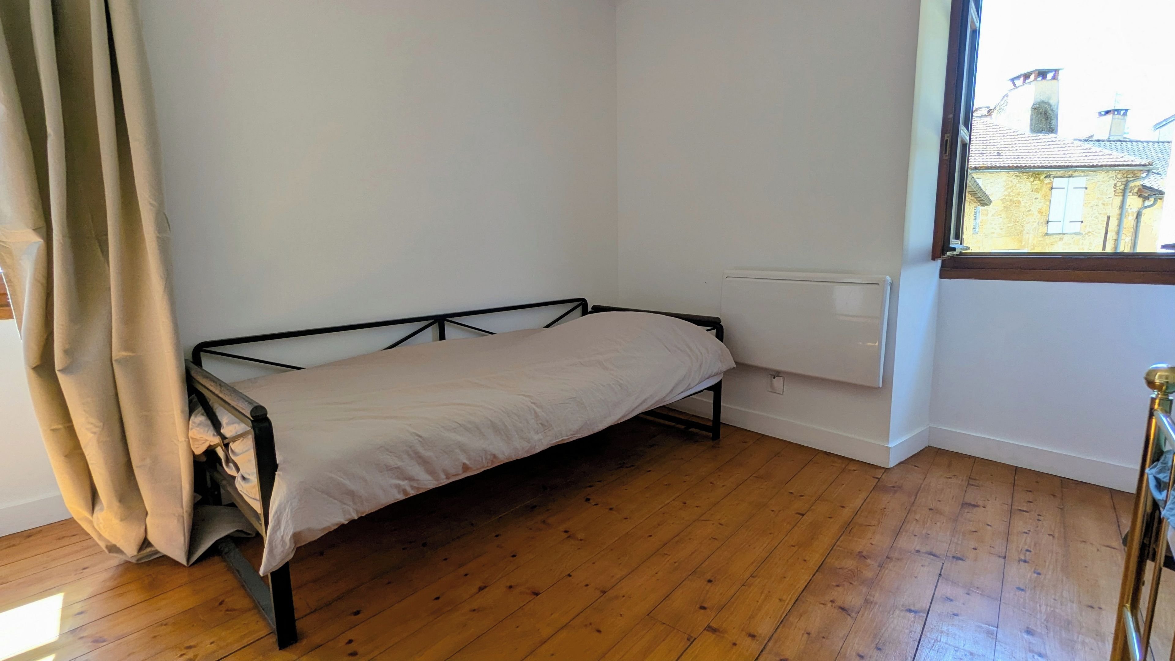 A room with a single bed, wooden flooring, a window with a view of buildings, and a radiator.