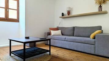 Uma sala de estar moderna com um sofá cinzento, uma mesa de centro, uma mesinha e uma estante de madeira com objetos decorativos.