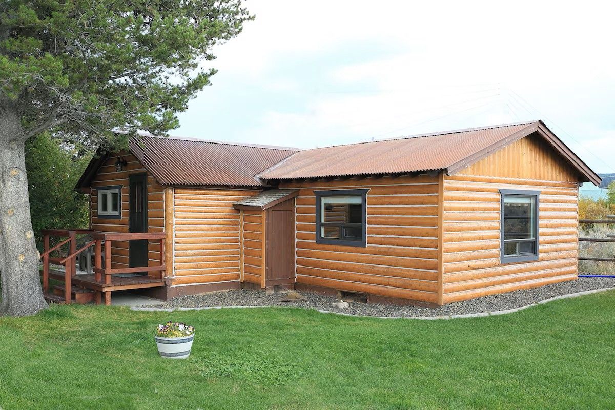 A log cabin with a porch, a small attached structure, and a grassy yard.